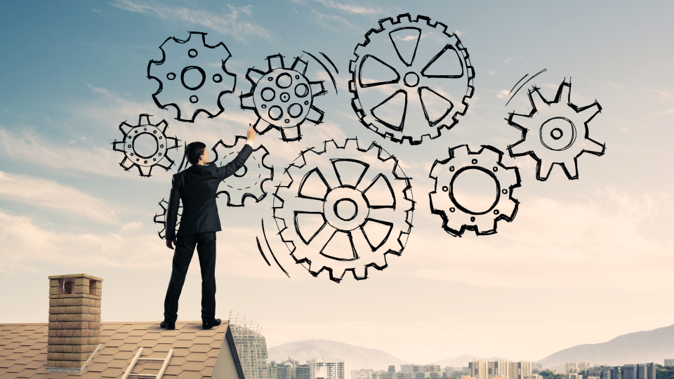 Business man standing on rooftop with hand drawn interconnected gears in the sky