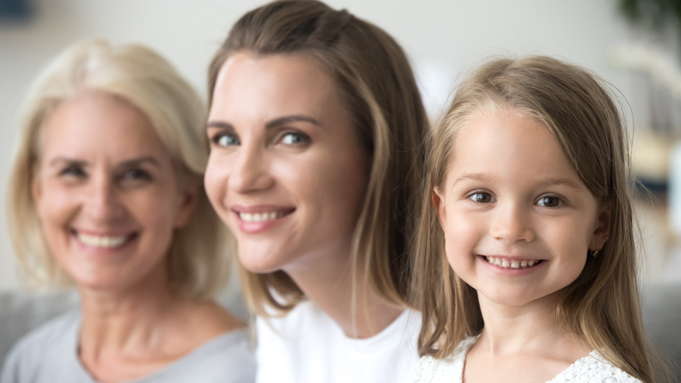 Three generations of women with young girl in focus on right, her mother partially out of focus in middle, and her mother blurred on the right